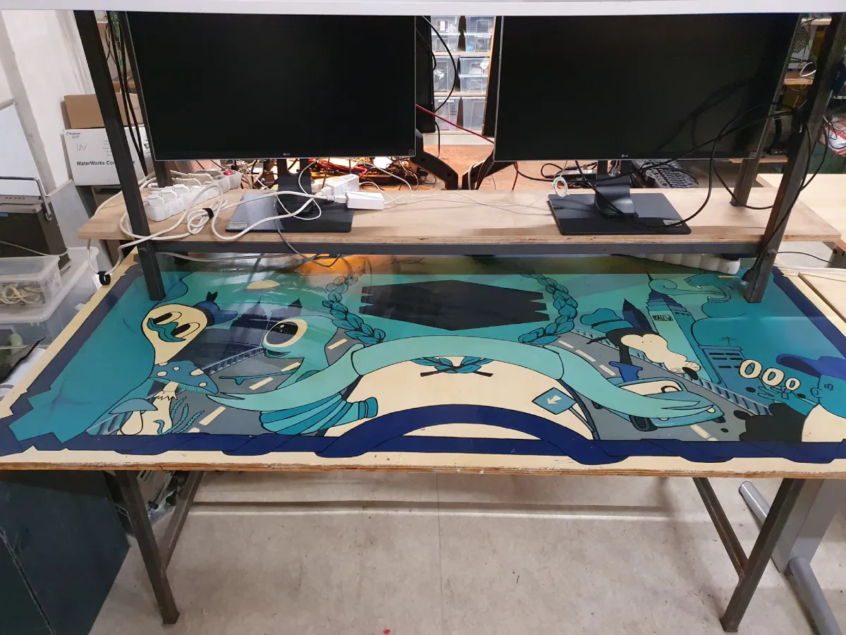Deep lore, core memories. A table with a colorful abstract motif in shades of blue and beige. There are two monitors and tangled cables on the table.